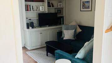 A living room with a teal sofa, a black coffee table, a white side table, and a wooden floor.