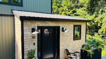 A small brick building with a black door and windows, a patio with a table and chairs, and a garden with plants.