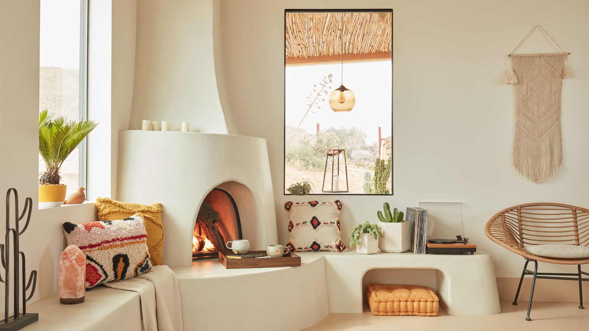 A cozy living room with a fireplace, a large window with a view of a desert landscape, and a macrame wall hanging.