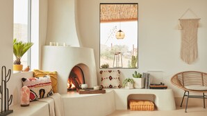 A cozy living room with a fireplace, a large window with a view of a desert landscape, and a macrame wall hanging. - 752 Ocean Ave  Unit A & B (Wells)