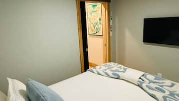 A bedroom with a bed, pillows, a ceiling fan, a wall-mounted TV, and a door leading to another room.