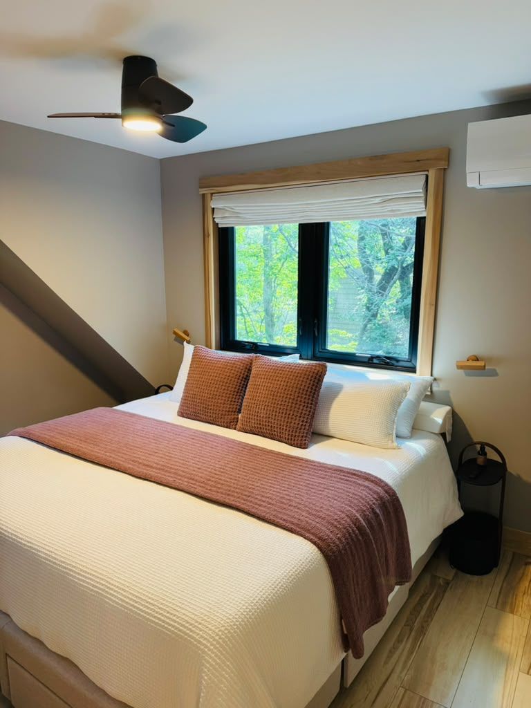 A bedroom with a bed, a ceiling fan, a window with blinds, and a bedside table.
