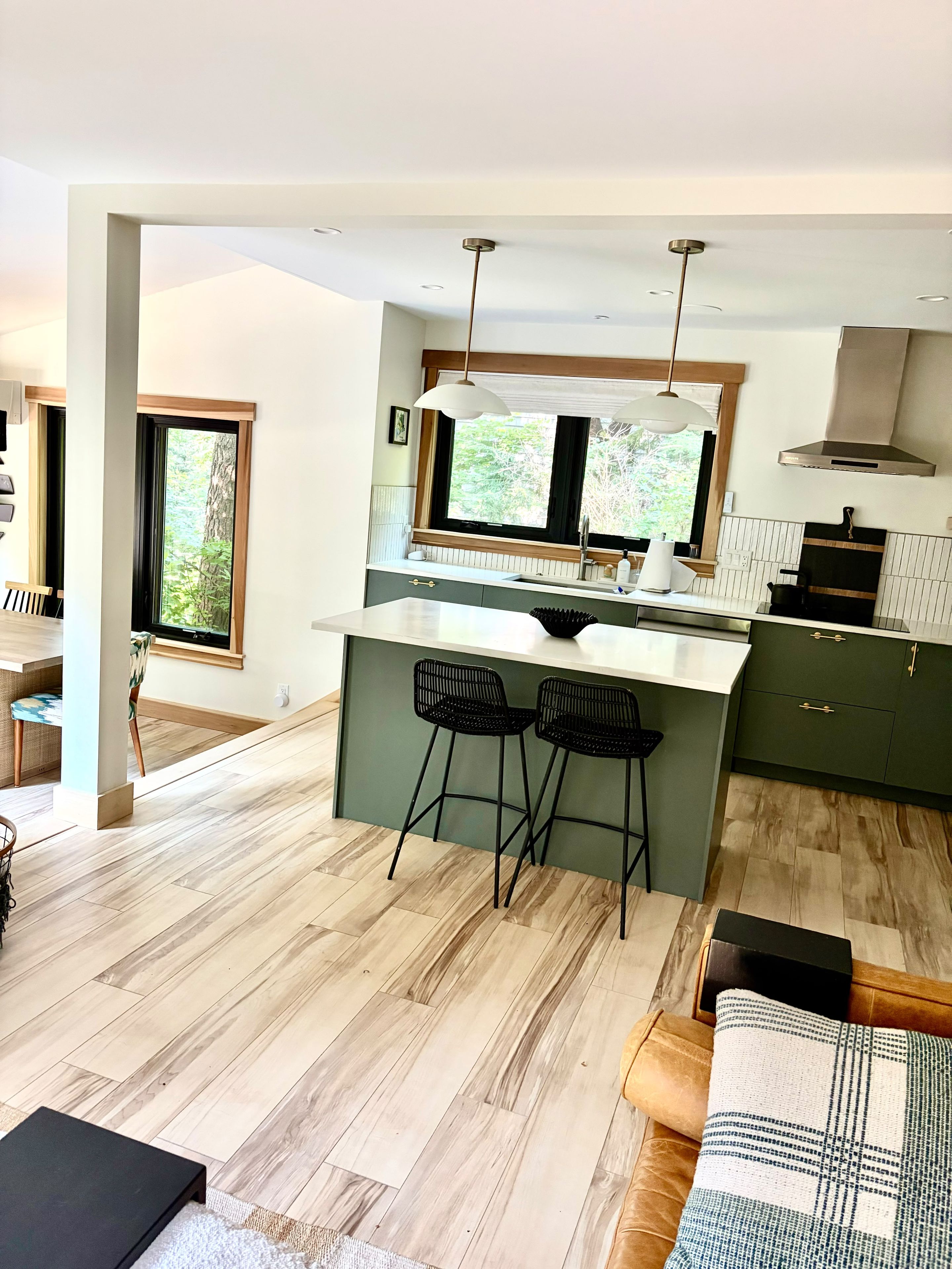 A modern kitchen with a central island, bar stools, and a view of greenery outside.