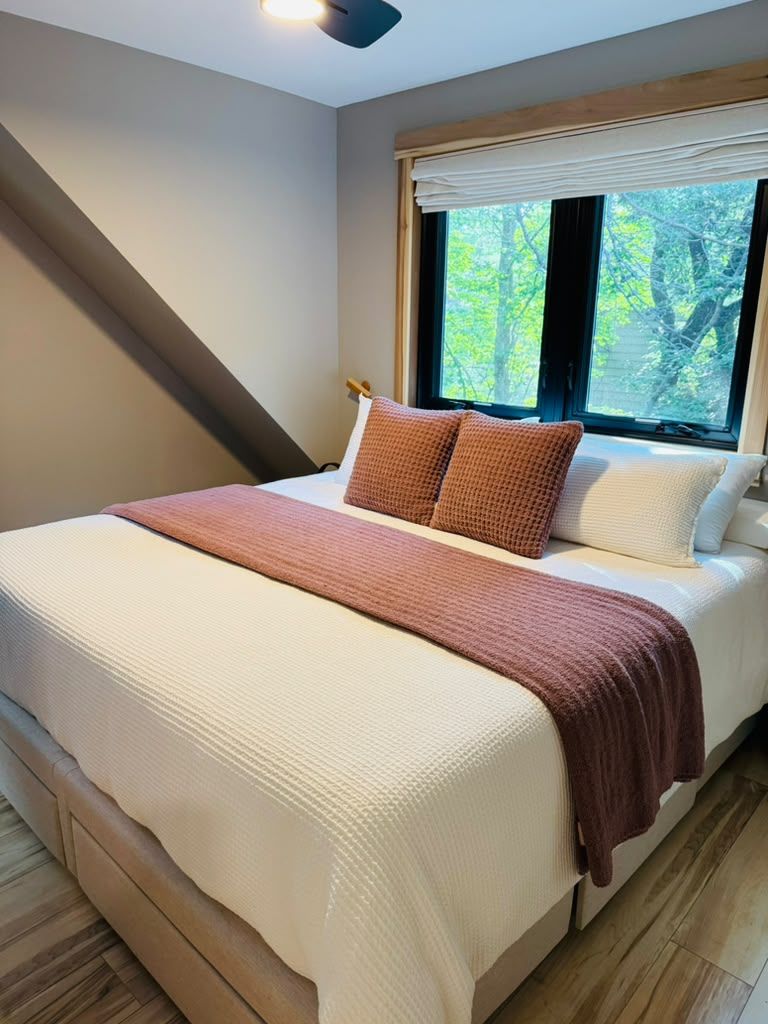 A bedroom with a bed, a window with blinds, and a sloped ceiling.