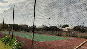 Uma quadra de tênis cercada, com superfície vermelha e linhas de demarcação verdes.