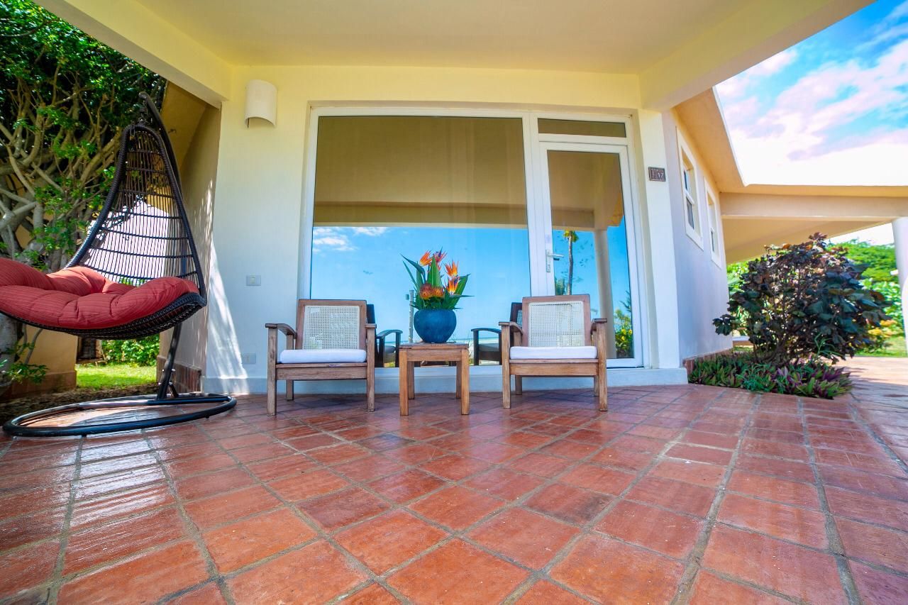 Une terrasse avec un fauteuil suspendu, deux chaises en bois, une table et une plante en pot.