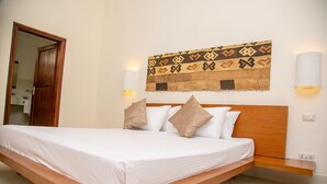 Uma cama com cabeceira de madeira, roupa de cama branca e duas luminárias fixadas na parede.