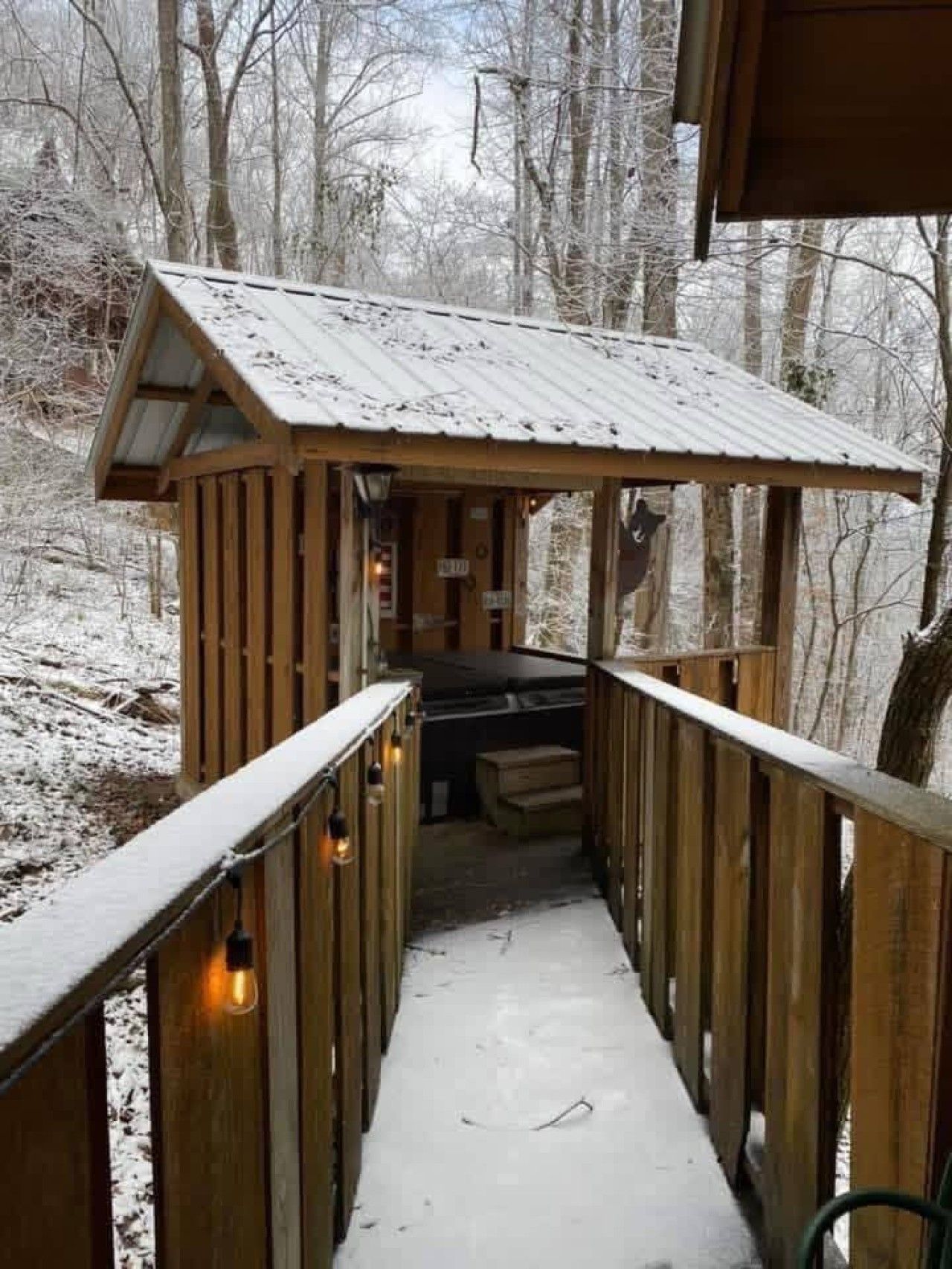 A wooden cabin with a metal roof, a bench, and a small table, surrounded by a snowy forest.