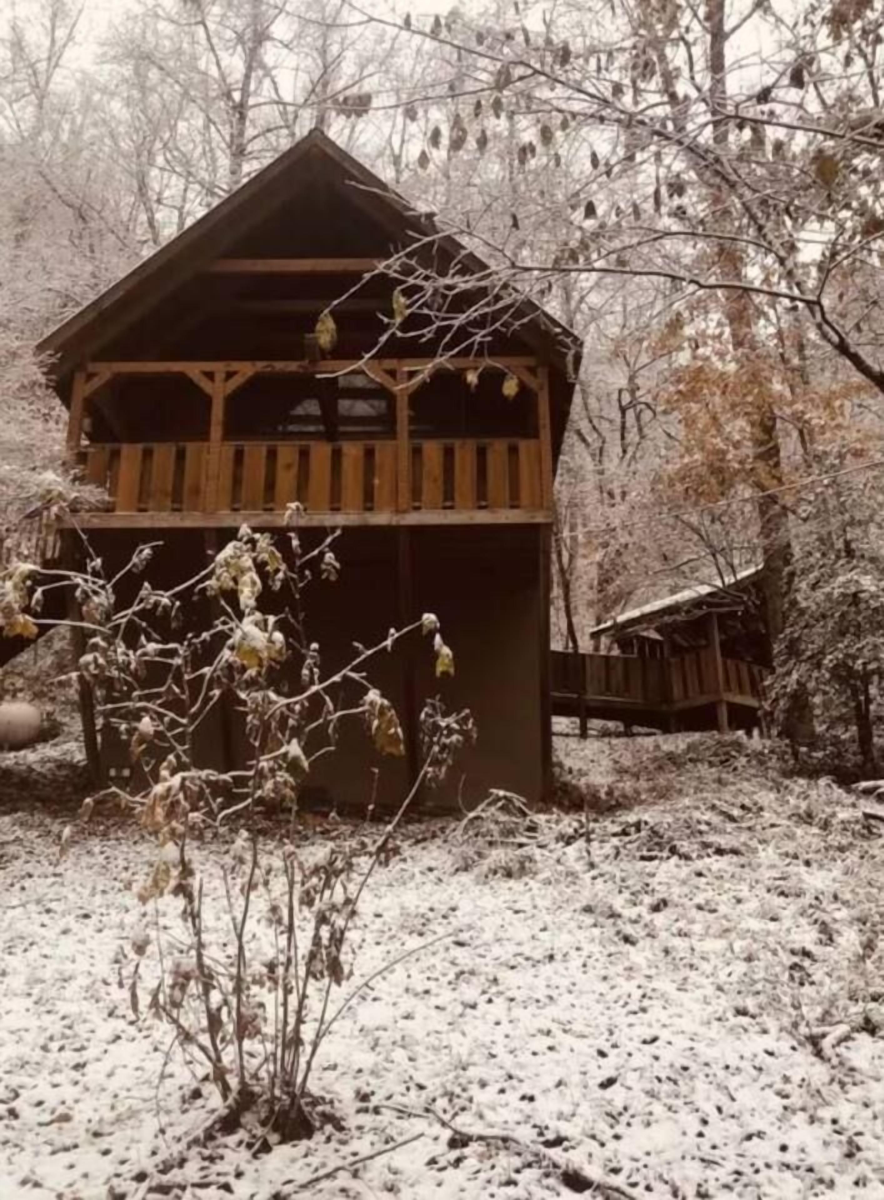 Una cabaña de madera con balcón, rodeada de nieve y árboles.
