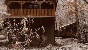 Una cabaña de madera con balcón, rodeada de nieve y árboles.