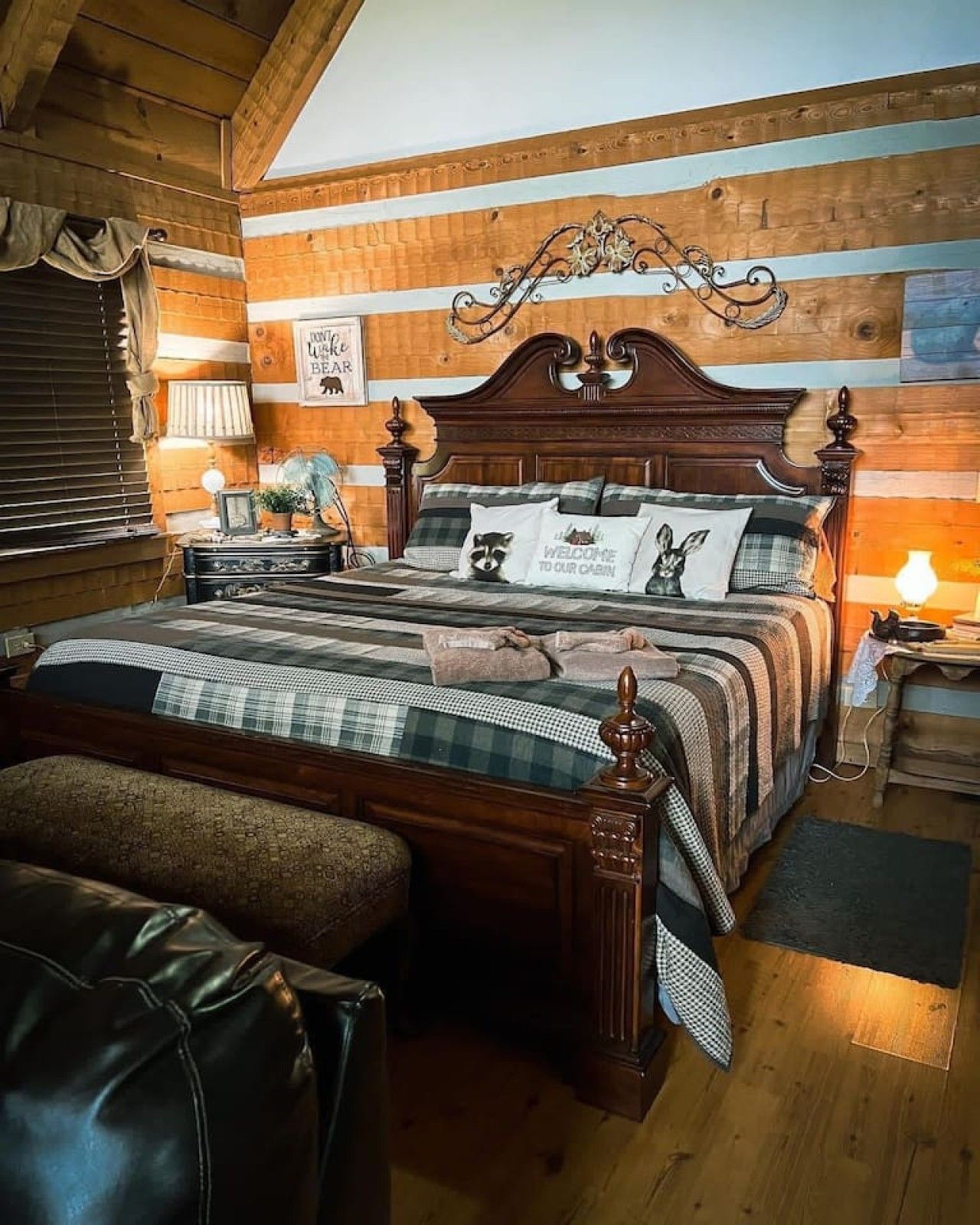 A wooden-paneled room with a large bed, a leather armchair, and a nightstand with a lamp.