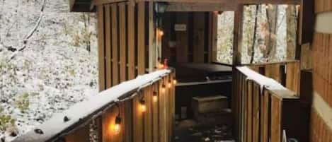A wooden deck with a snow-covered path leading to a building, surrounded by trees.