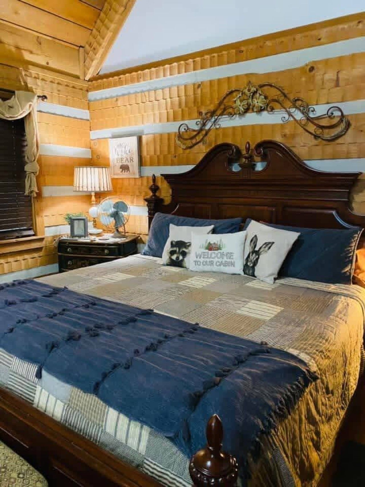 A wooden cabin bedroom with a large bed, a nightstand, a lamp, and a decorative wall piece.