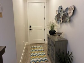A hallway with a white door, a patterned rug, a potted plant, a decorative wall piece, and a cabinet with a bowl on top. - Enjoyable townhome in gorgeous Washington with a great location (Washington)