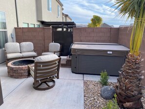 A patio area with a hot tub, two cushioned chairs, a fire pit, and a small garden with rocks and a palm tree. - Enjoyable townhome in gorgeous Washington with a great location (Washington)