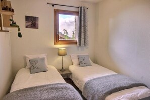 A small, cozy bedroom with two beds, a nightstand with a lamp, a window with curtains, and a wall-mounted shelf with decorative items. - Chalet, 200m from ski lifts, balcony, fireplace or stove, tv, ski locker, 98m², Peisey-Vallandry (Landry)