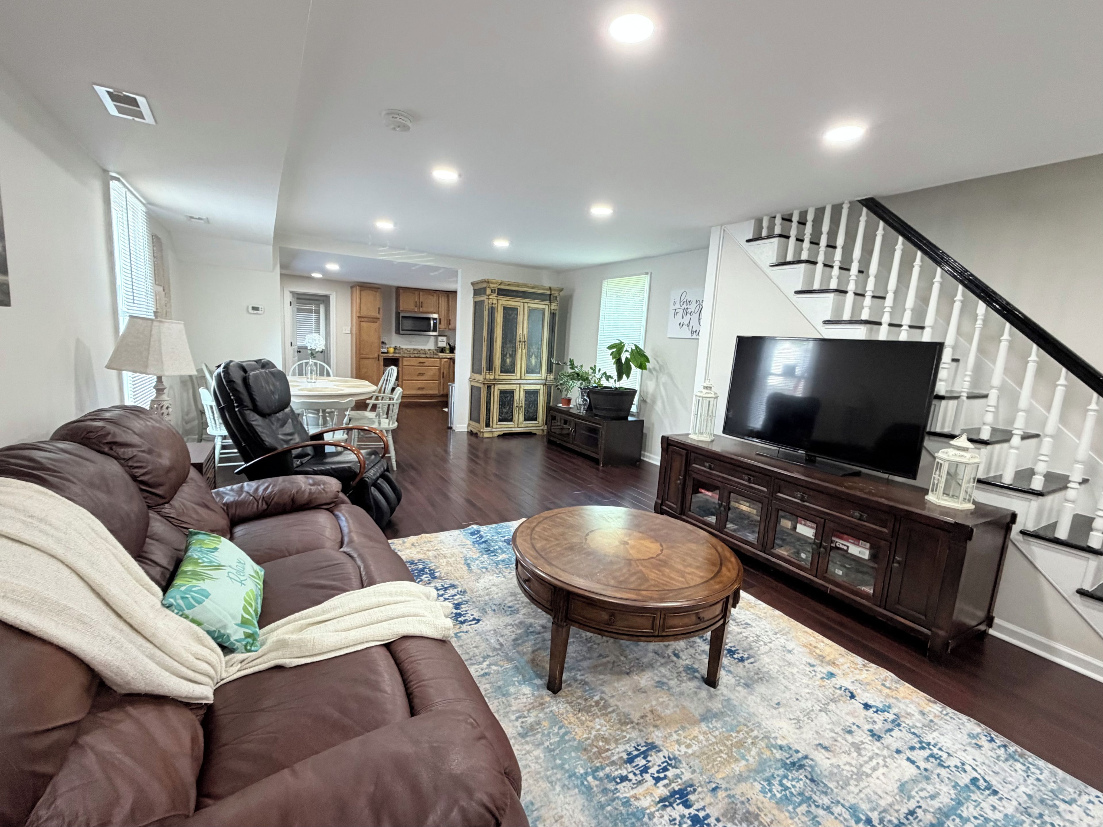 A living room with a brown leather sofa, a wooden coffee table, and a large flat-screen TV on a wooden stand.