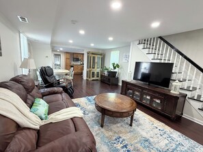 A living room with a brown leather sofa, a wooden coffee table, and a large flat-screen TV on a wooden stand.
