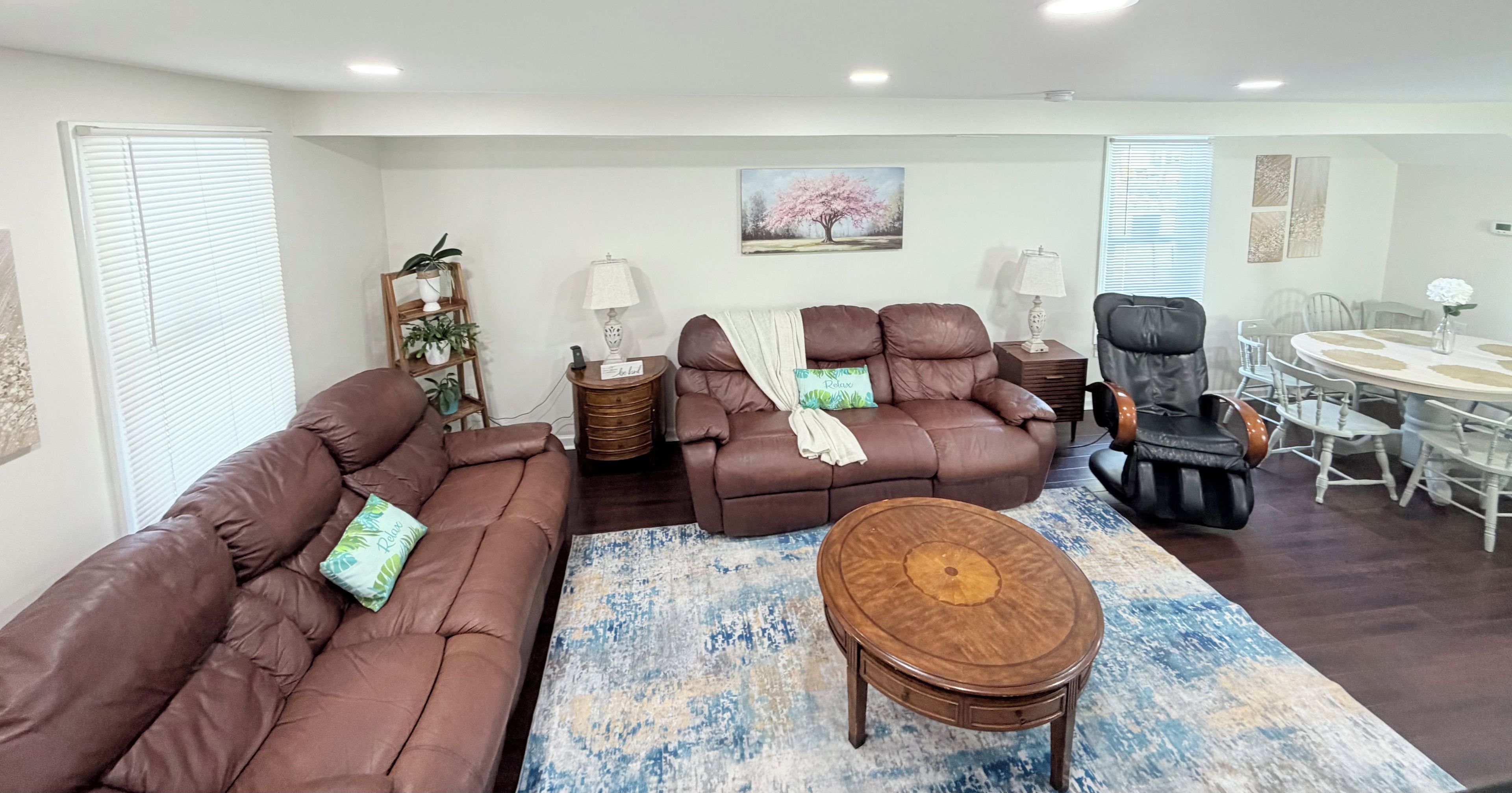 A living room with a brown sofa set, a massage chair, a round wooden coffee table, and a dining area with a white table and chairs.