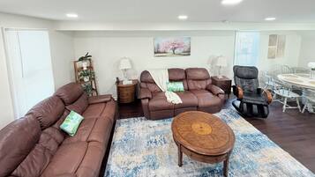 A living room with a brown sofa set, a massage chair, a round wooden coffee table, and a dining area with a white table and chairs.