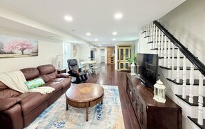 Un salon avec un canapé en cuir marron, une table basse ronde en bois, un téléviseur et un escalier avec des balustrades blanches.