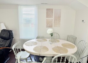 A dining area with a round table, white chairs, a vase with flowers, and artwork on the wall.