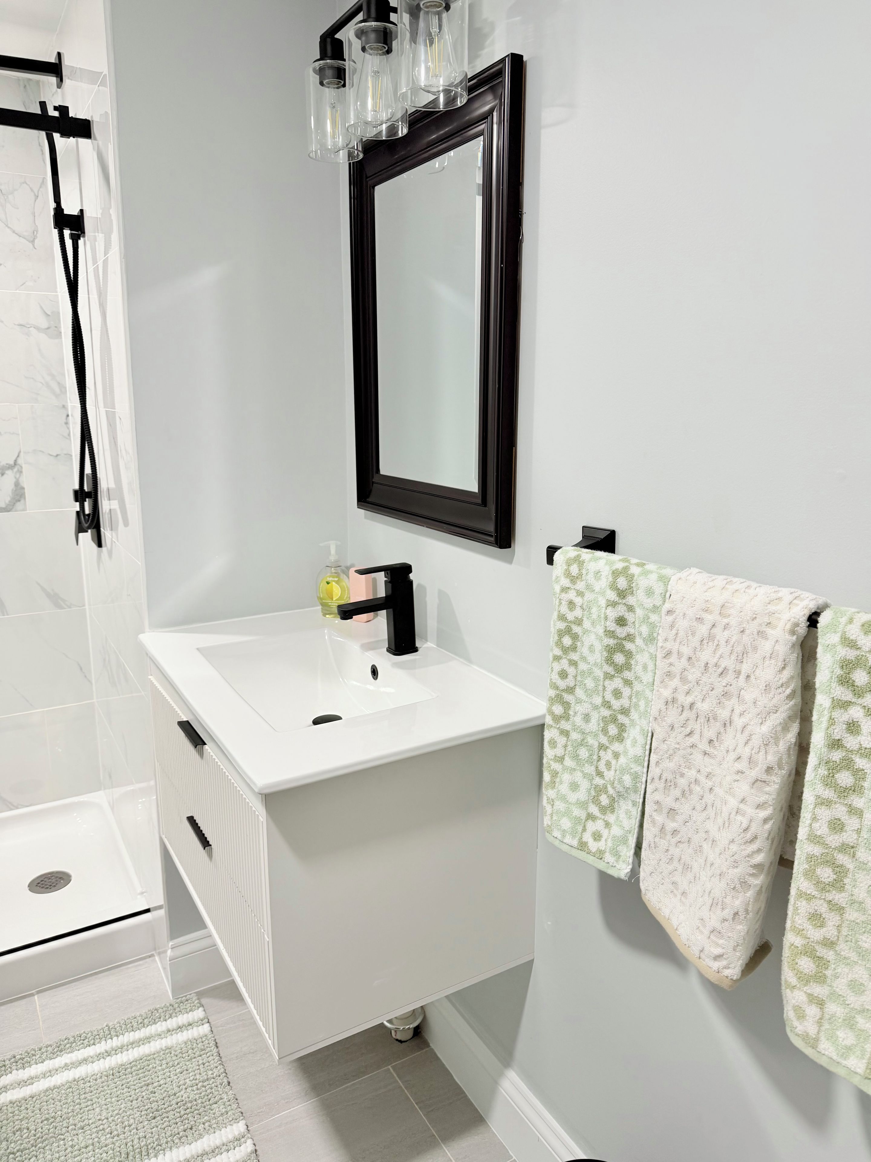 Une salle de bain moderne avec un lavabo blanc, un miroir à cadre noir et un porte-serviettes orné de serviettes à motifs.