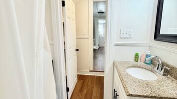 A bathroom with a white bathtub, a sink with a granite countertop, and a shower curtain.