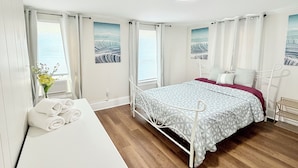 A bedroom with a bed, a bedside table, a window with curtains, and a view of the sea. - More, than just a place to sleep - welcome home! (Cambridge)