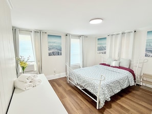 Ein Schlafzimmer mit Bett, Nachttisch, Fenster mit Vorhängen und Meerblick.