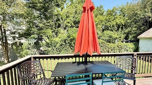 A deck with a table and chairs, a red umbrella, and a wooden railing. - More, than just a place to sleep - welcome home! (Cambridge)