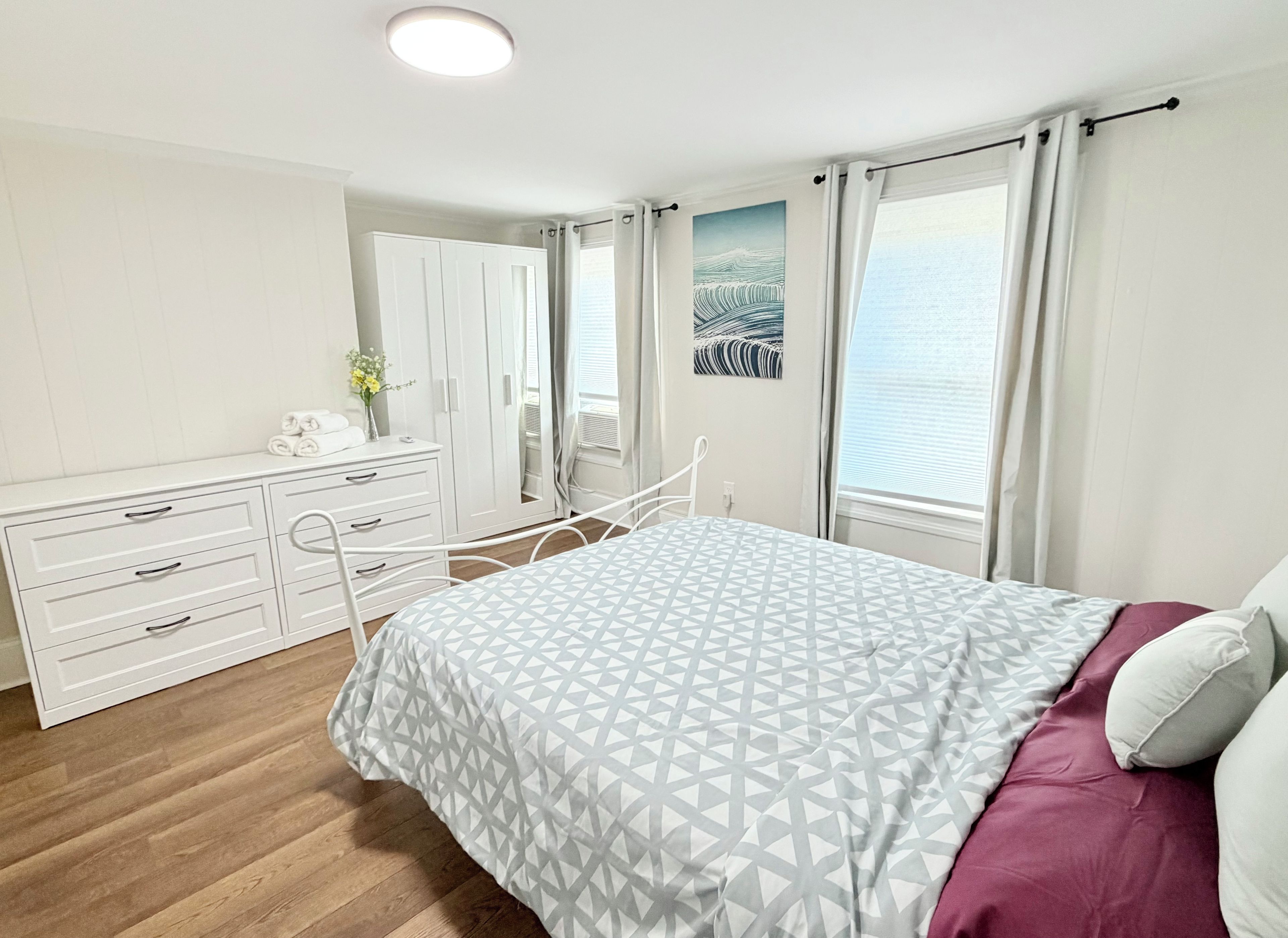 Une chambre à coucher avec un lit, une commode, un miroir et une fenêtre avec des rideaux.