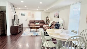 A spacious living room with a brown leather sofa, a round coffee table, and a dining area with a white table and chairs. - More, than just a place to sleep - welcome home! (Cambridge)