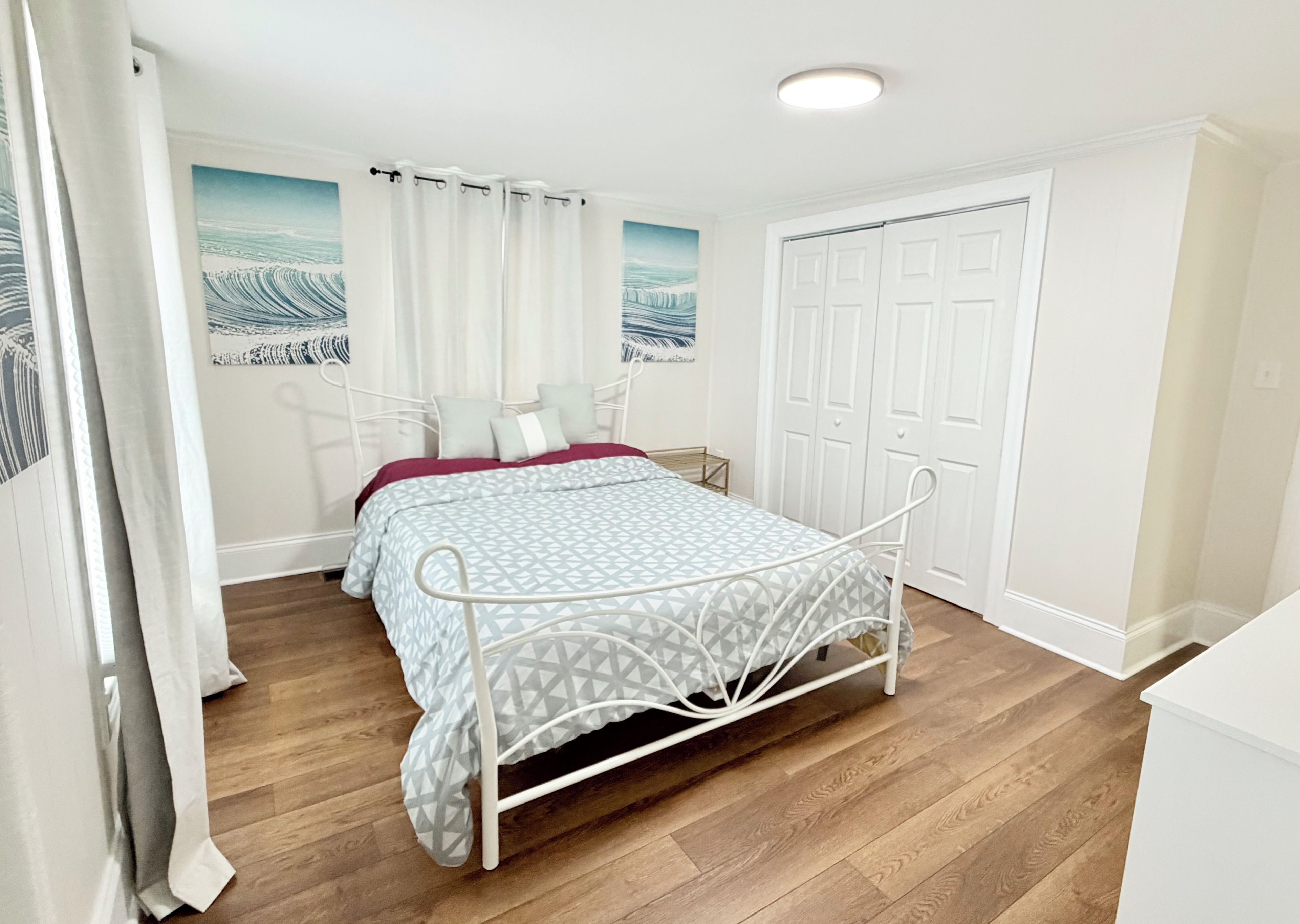 A bedroom with a metal bed frame, a wooden floor, a white door, and a painting on the wall.