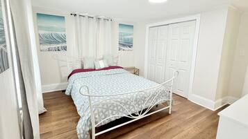 A bedroom with a metal bed frame, a wooden floor, a white door, and a painting on the wall.