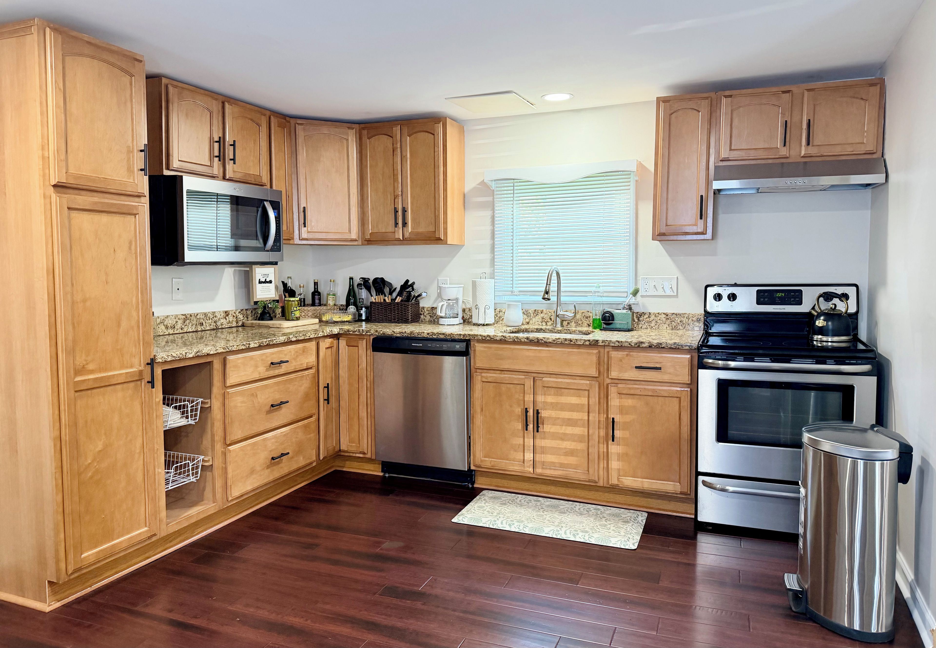 Una cocina con armarios de madera, un refrigerador de acero inoxidable, un microondas, un lavavajillas, una estufa y un cubo de basura.