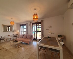 A modern living room with a sofa, coffee table, dining table, and chairs. There are two pendant lights, a mirror, and a clock on the wall. - Relax, unwind and enjoy your own private villa in the Costa Papagayo area. (Playa Blanca)