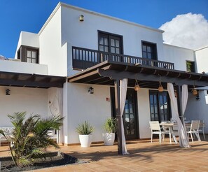 A modern two-story building with a balcony, potted plants, and outdoor seating. - Relax, unwind and enjoy your own private villa in the Costa Papagayo area. (Playa Blanca)