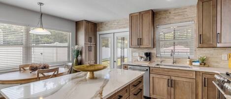Una cocina moderna con armarios de madera, encimera de mármol y comedor con mesa y sillas redondas.