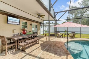 Une terrasse extérieure avec une piscine, un coin repas doté de meubles en bois et un ventilateur de plafond.