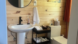 Een badkamer met een houten wand, een ronde spiegel, een witte wastafel, een zwart plankje met handdoeken en een toilet.
