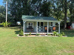 A small house with a porch, a bench, and two chairs.