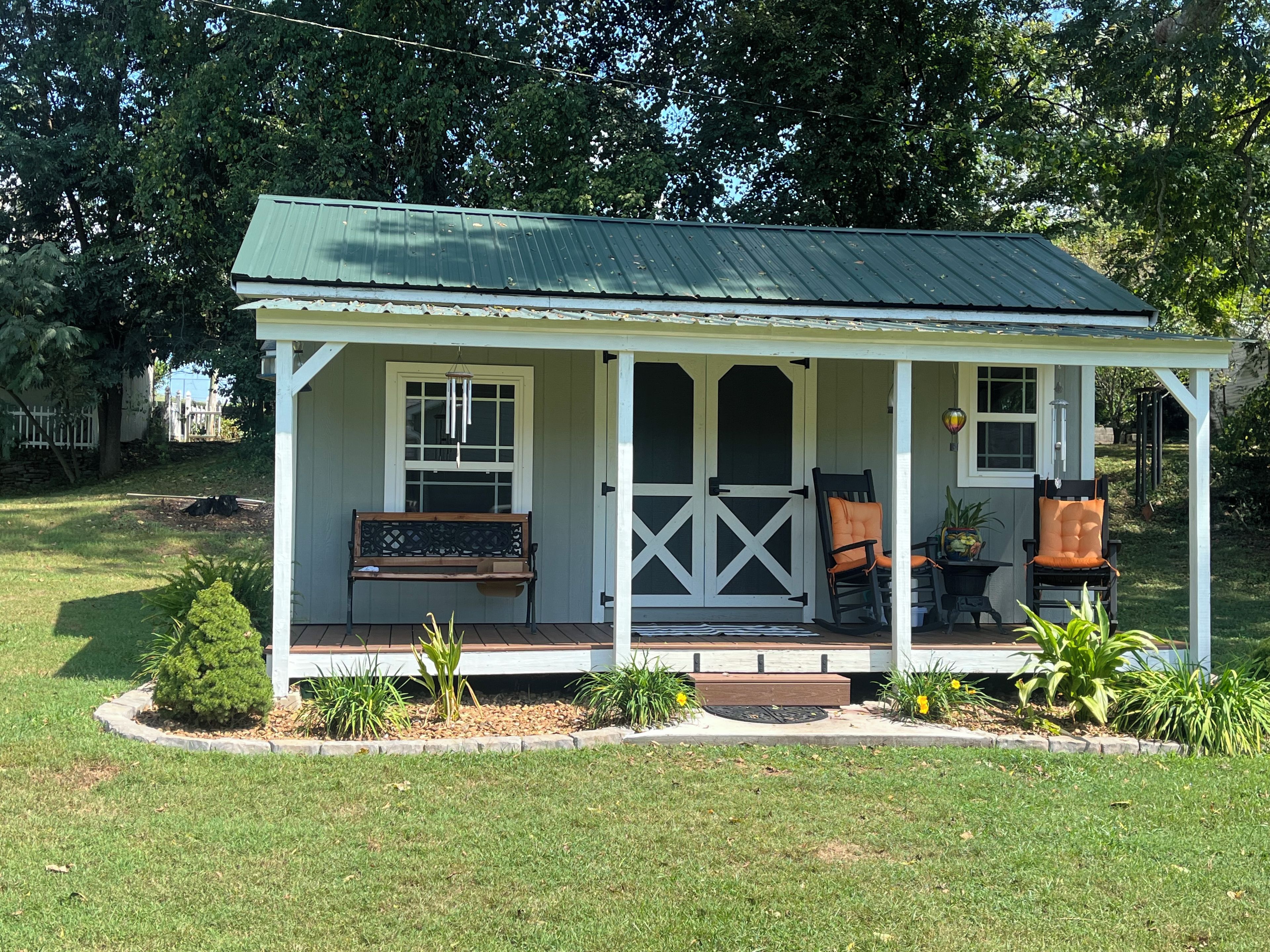 Een klein, gelijkvloers huis met een veranda, een bank en twee stoelen.