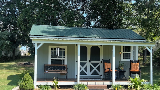 Een klein, gelijkvloers huis met een veranda, een bank en twee stoelen.