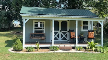 Een klein, gelijkvloers huis met een veranda, een bank en twee stoelen.