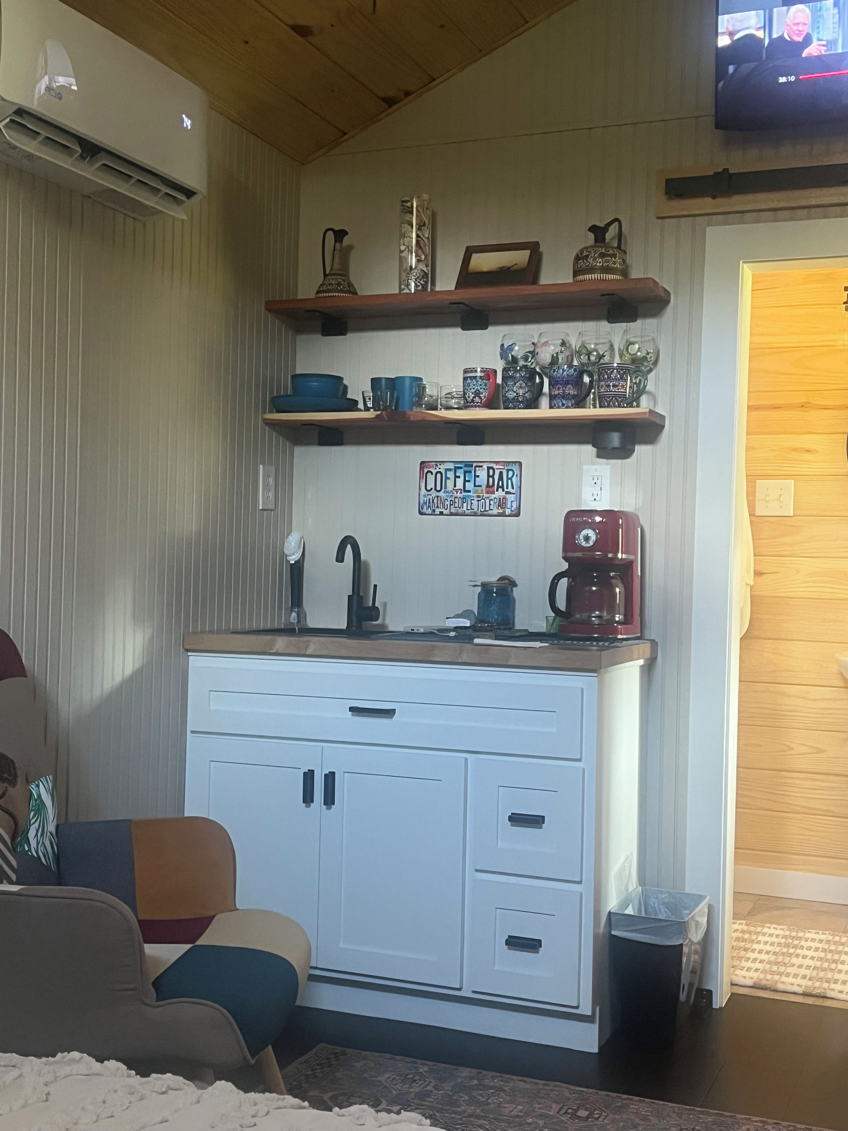 A compact kitchen area with a coffee bar sign, a coffee maker, and various kitchen utensils.