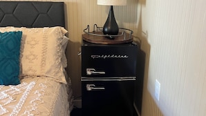 Een slaapkamer met een bed, nachtkastje, lamp en een dressoir.