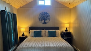 Een slaapkamer met een bed, twee nachtkastjes, een wanddecoratie van een boom en een raam met gordijnen.