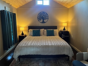 Een slaapkamer met een bed, twee nachtkastjes, een wanddecoratie van een boom en een raam met gordijnen.