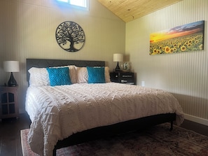 Un dormitorio con cama, mesita de noche, lámpara, cómoda, una obra de arte en la pared y alfombra.